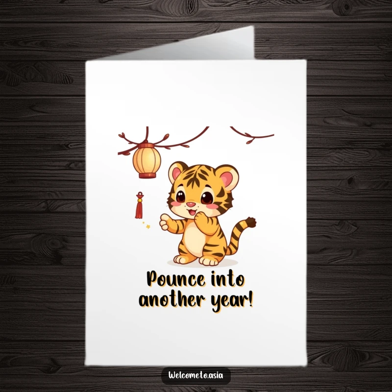 Funny free printable birthday card of an adorable tiger cub playfully swatting at a glowing dangling lantern, full of mischievous energy.